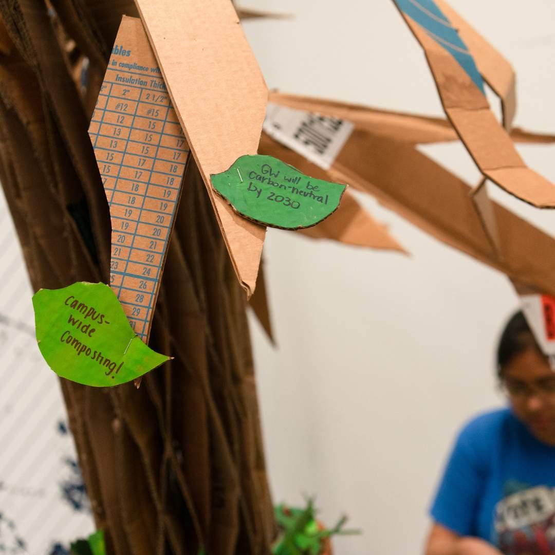 A cardboard tree with leaves that have GW sustainability facts written on them