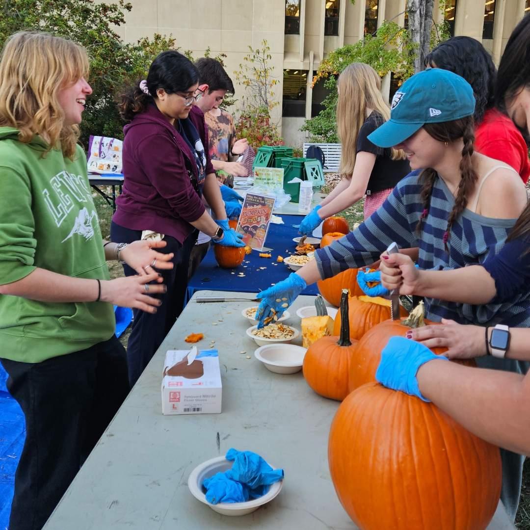 students carve pumpkins at a table on campus